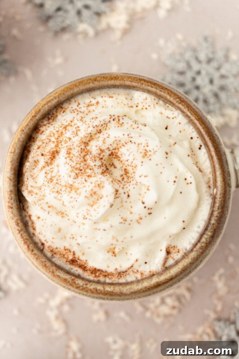 An inviting overhead shot of a mug filled with creamy snowman soup, generously topped with whipped cream and a festive sprinkle of cinnamon, ready to be enjoyed.