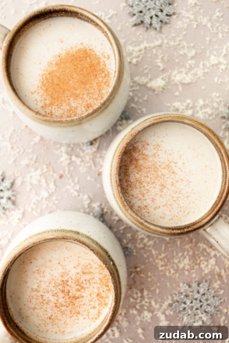 Several mugs of warm vanilla milk, each topped with fluffy whipped cream and a sprinkle of cinnamon, creating a festive display.