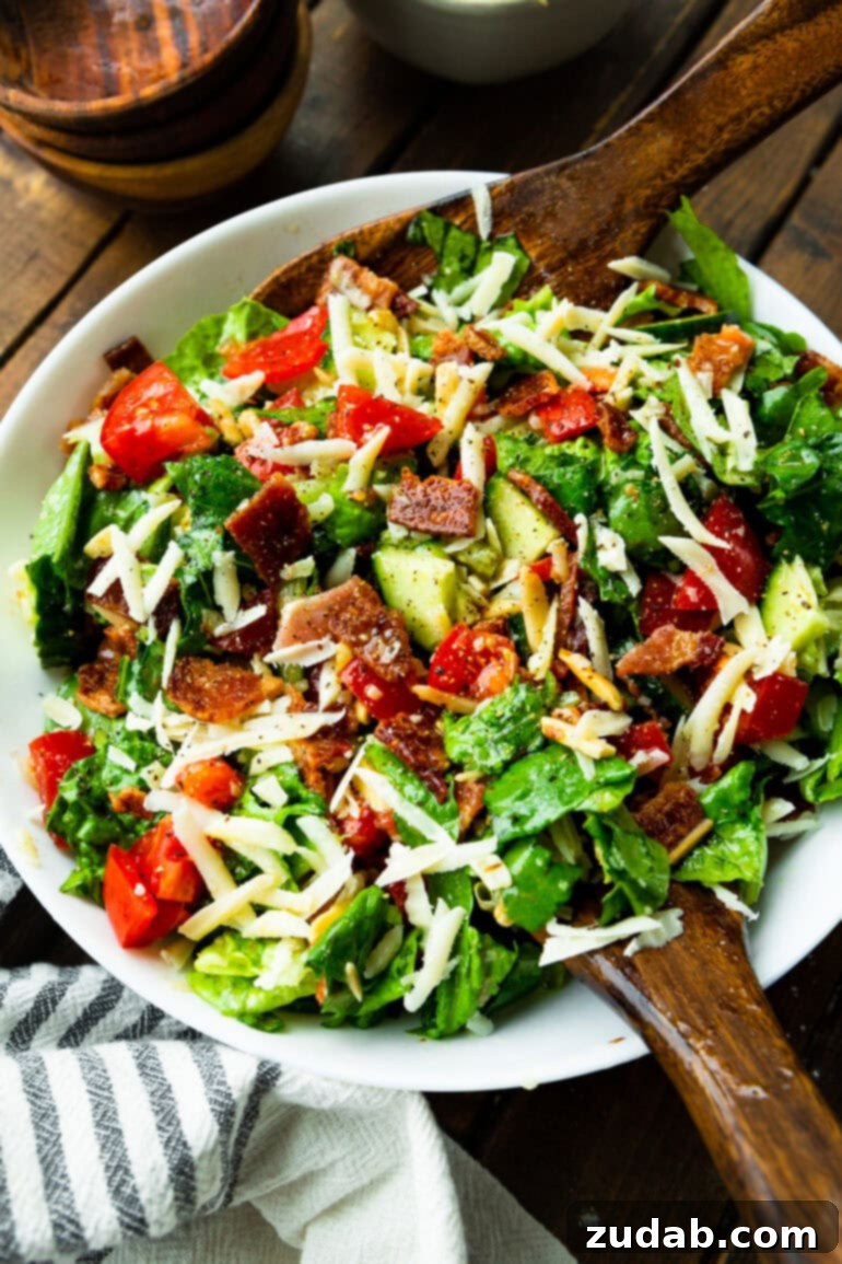 The Ultimate House Salad Recipe 2 A large bowl brimming with a vibrant green salad, featuring slivered almonds, juicy red tomatoes, and savory bacon crumbles, all perfectly tossed for a mouthwatering presentation.
