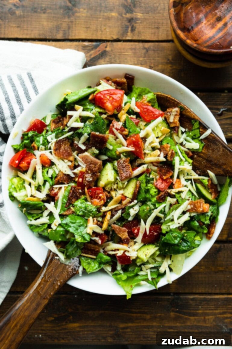 The Ultimate House Salad Recipe 3 A large serving bowl filled with a delightful mix of chopped romaine lettuce, ripe tomatoes, crunchy slivered almonds, refreshing cucumber, and savory shredded Manchego cheese, ready to be dressed.