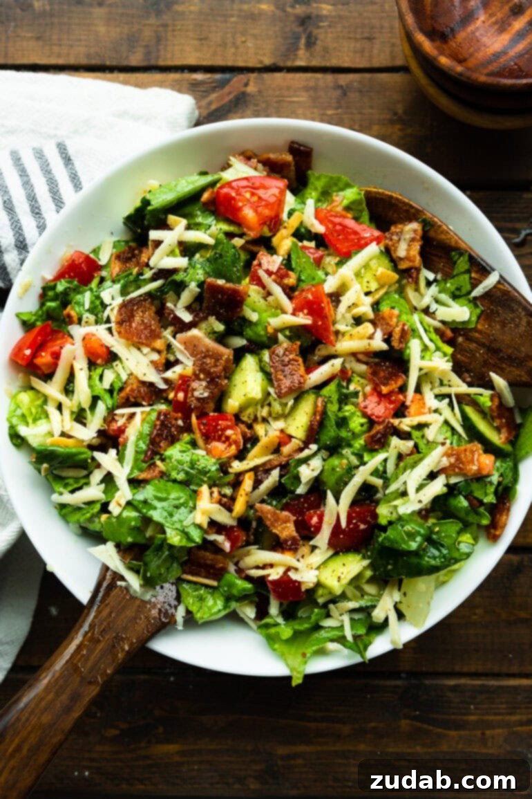 The Ultimate House Salad Recipe 6 A vibrant green salad, perfectly tossed with juicy tomatoes, crispy bacon crumbles, refreshing cucumber slices, and a generous drizzle of zesty lemon vinaigrette, presented in a clear glass bowl.