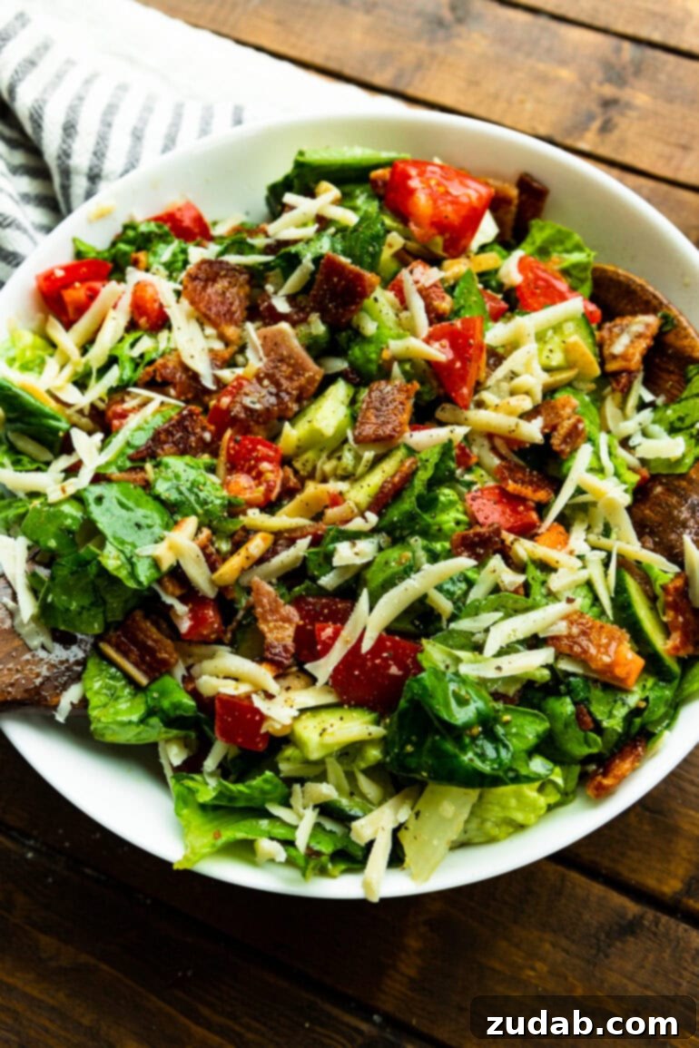 The Ultimate House Salad Recipe 7 A perfectly tossed green salad featuring crunchy slivered almonds, vibrant tomatoes, savory Manchego cheese, and irresistible crispy bacon crumbles, all glistening with a delicious dressing.