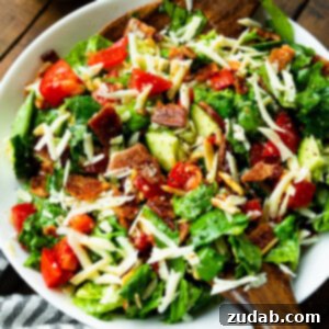a photo of a large bowl full of a green salad with slivered almonds, tomatoes, and bacon crumbles