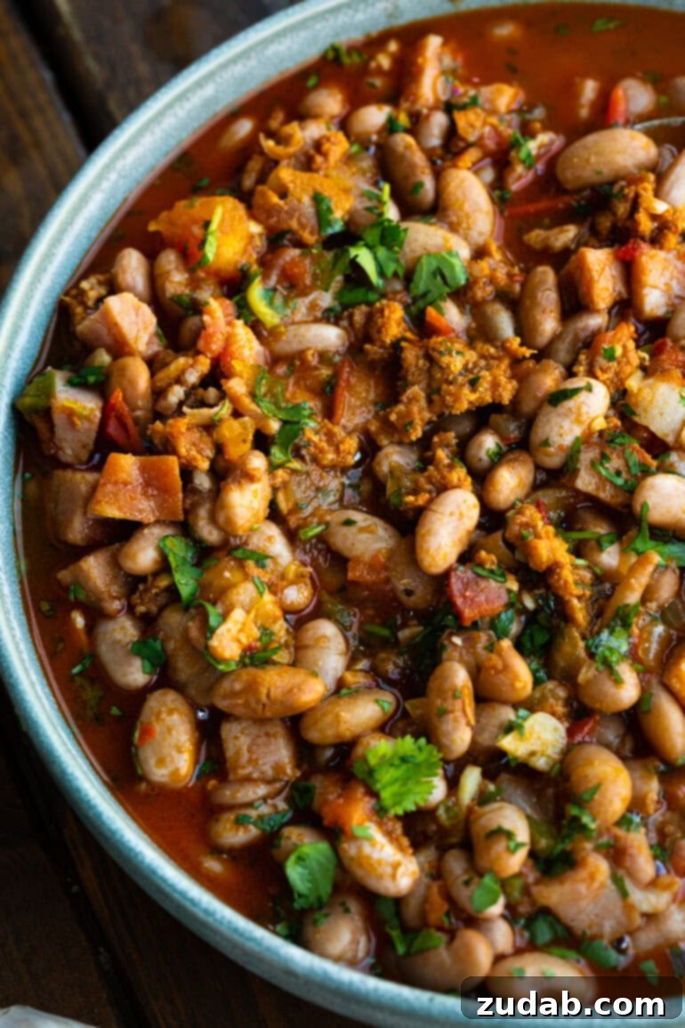 Classic Charro Beans Recipe 3 An overhead view of a large, rustic bowl brimming with charro beans, loaded with chunks of ham, bacon, and chorizo, all generously garnished with fresh cilantro.