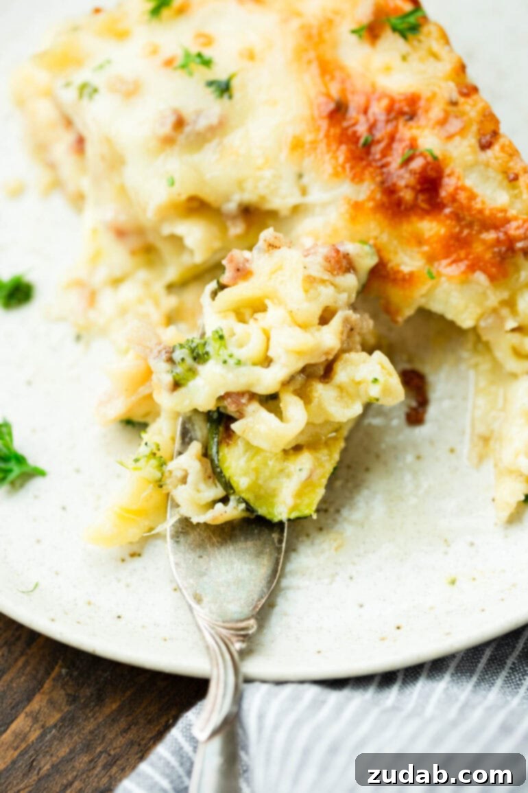 Creamy Vegetable Lasagna with Crispy Pancetta 11 A close-up of a slice of pancetta vegetable lasagna with white sauce being enjoyed with a fork, showing its rich and creamy texture.