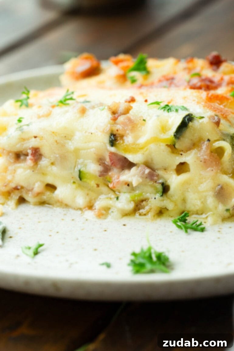 Creamy Vegetable Lasagna with Crispy Pancetta 7 A close-up photo of a perfectly portioned piece of pancetta vegetable lasagna with white sauce, served on a white dinner plate, highlighting its cheesy layers.