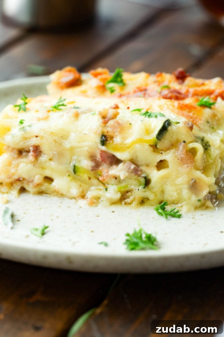 Creamy Vegetable Lasagna with Crispy Pancetta 10 A side view of a slice of pancetta vegetable lasagna with white sauce on a dinner plate, revealing its many cheesy, layered components.