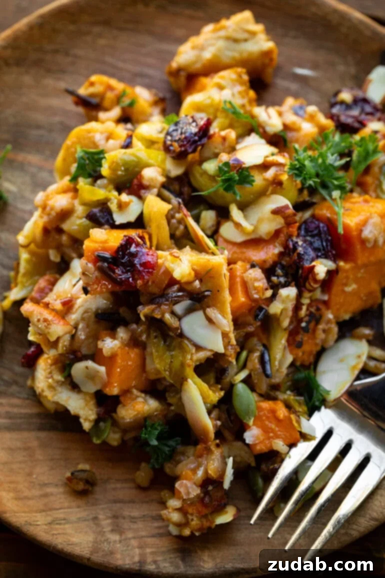 Nourishing Chicken Harvest Bake 3 A close-up photo of a serving of Harvest Chicken Casserole on a rustic wood dinner plate with a fork, showing the rich textures of chicken, sweet potatoes, and Brussels sprouts