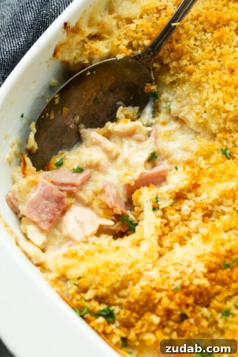 Creamy Chicken Cordon Bleu Casserole 3 A large serving spoon scooping out a generous portion of creamy Chicken Cordon Bleu Casserole, revealing layers of chicken, ham, and Swiss cheese beneath a crispy panko topping.