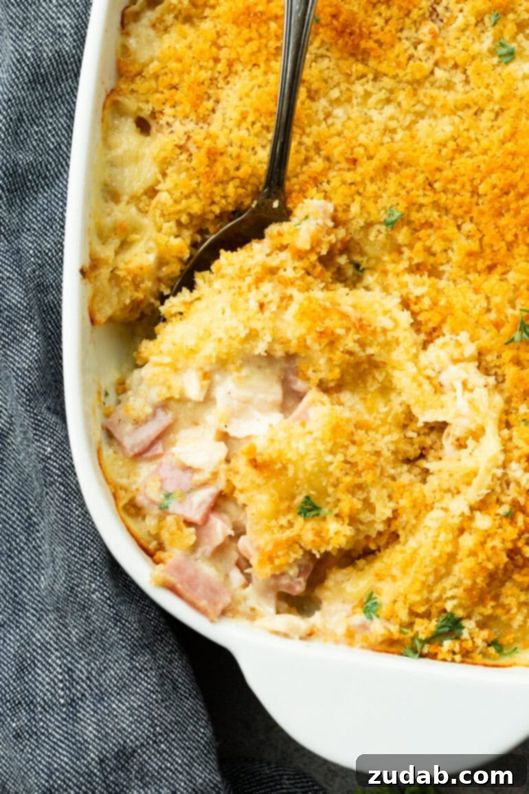 Creamy Chicken Cordon Bleu Casserole 8 A large serving spoon scooping out a portion of creamy Chicken Cordon Bleu Casserole from a white baking dish.
