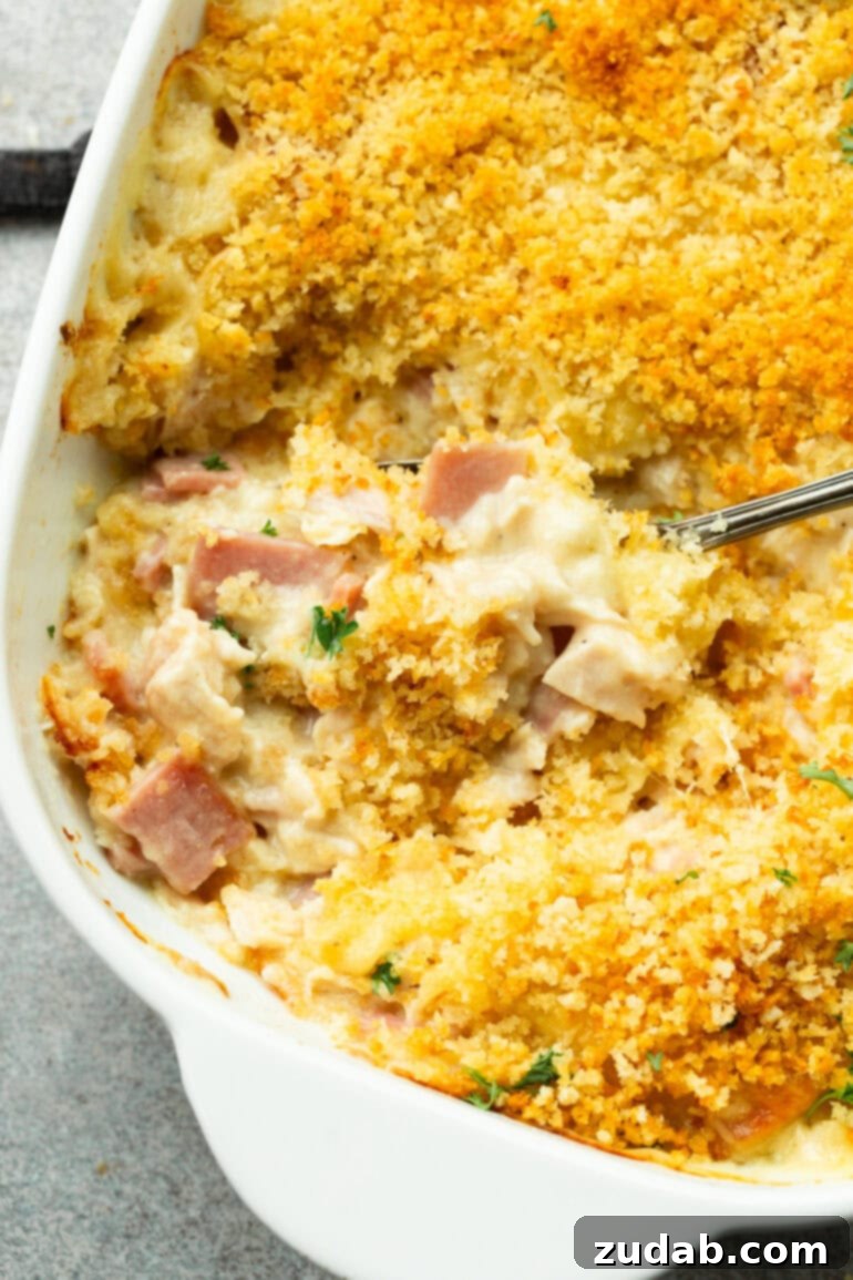 Creamy Chicken Cordon Bleu Casserole 10 A close-up shot of someone scooping up a serving of creamy Chicken Cordon Bleu Casserole from a large baking dish.