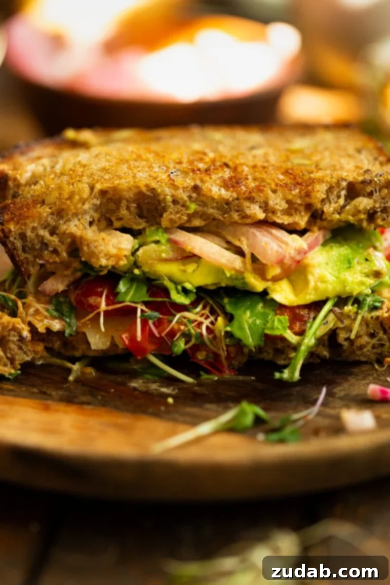 My Signature Avocado Sandwich 2 A vibrant avocado sandwich on toasted multigrain bread, featuring creamy avocado slices, bright red pickled onions, fresh bean sprouts, crisp arugula, and juicy charred tomatoes. Perfect for a healthy, gourmet lunch.