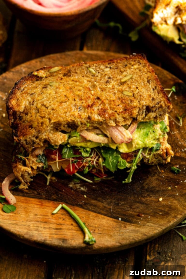 My Signature Avocado Sandwich 11 A beautifully presented half of an avocado sandwich on toasted multigrain bread, served on a wooden plate, ready to be enjoyed. It highlights the golden toast and fresh green fillings.