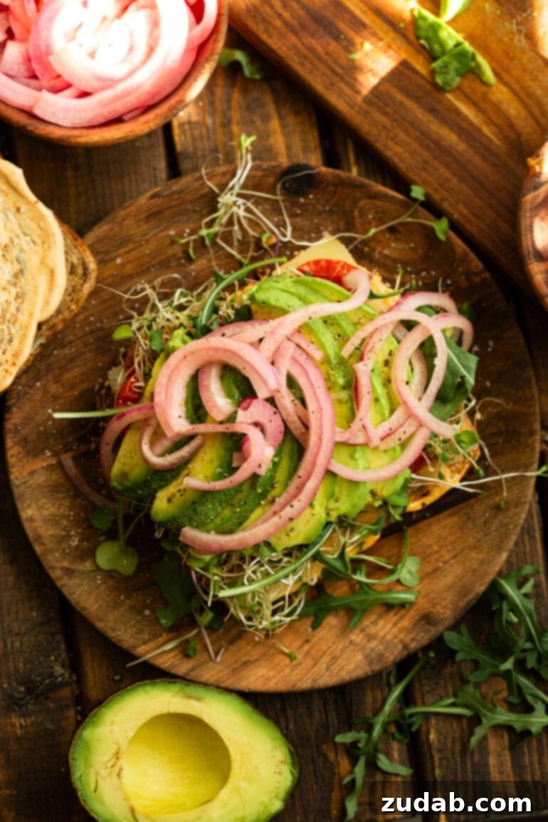 My Signature Avocado Sandwich 10 An open-faced avocado sandwich showing the artfully arranged ingredients: perfectly sliced avocado, vibrant pickled red onions, delicate microgreens, and crisp bean sprouts, all nestled on a slice of toasted bread.