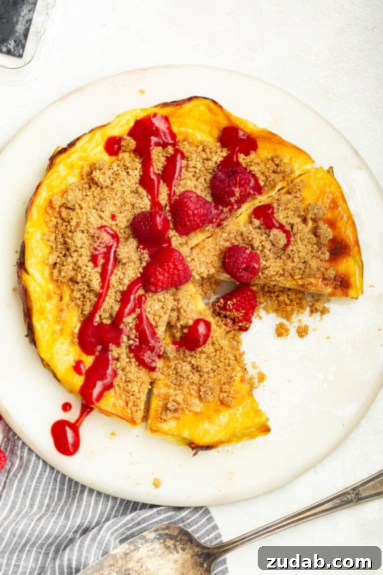 Baked Yogurt Cheesecake 7 An inviting overhead view of a large Cheesecake Baked Yogurt, with a slice missing, revealing its creamy interior. It's garnished with vibrant raspberry sauce, a crunchy graham cracker crumble, and fresh whole raspberries.