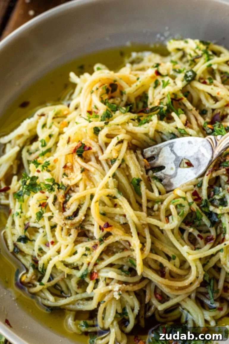 Flavorful Aglio e Olio Made Easy 5 A fork twirling cooked spaghetti pasta, richly coated with sizzling oil and a medley of fresh herbs