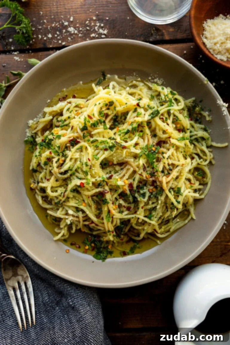 Flavorful Aglio e Olio Made Easy 7 A large serving bowl full of cooked spaghetti, tossed generously with olive oil, fresh herbs, and grated Parmesan cheese