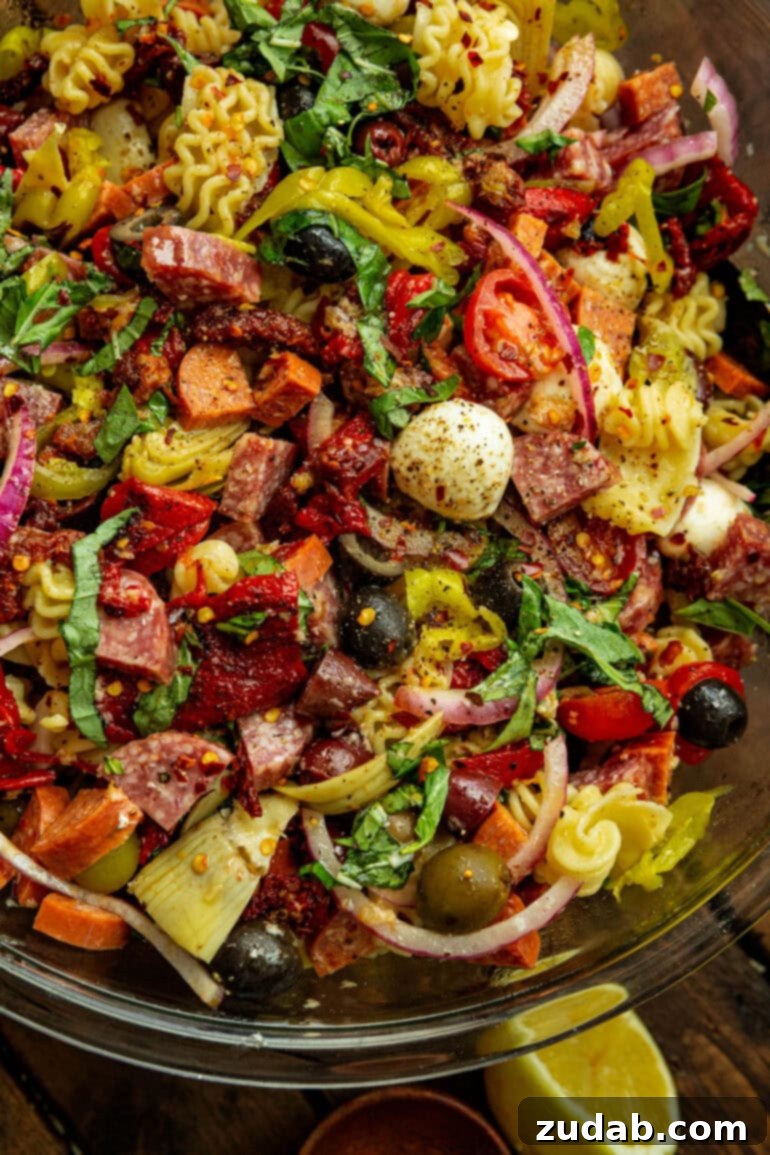 Effortless Antipasto Pasta Salad Recipe 2 A vibrant antipasto pasta salad in a large glass bowl, featuring cooked rotini pasta, mozzarella pearls, sliced pepperoncini, salami, pepperoni, and a mix of olives, all ready to be served.