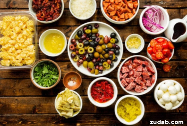 Effortless Antipasto Pasta Salad Recipe 4 A high-angle photo displaying all the individual ingredients for an antipasto pasta salad, neatly arranged in separate small bowls, including various olives, chunks of salami and pepperoni, fresh basil leaves, artichoke hearts, roasted red peppers, and more, highlighting the fresh and diverse components.