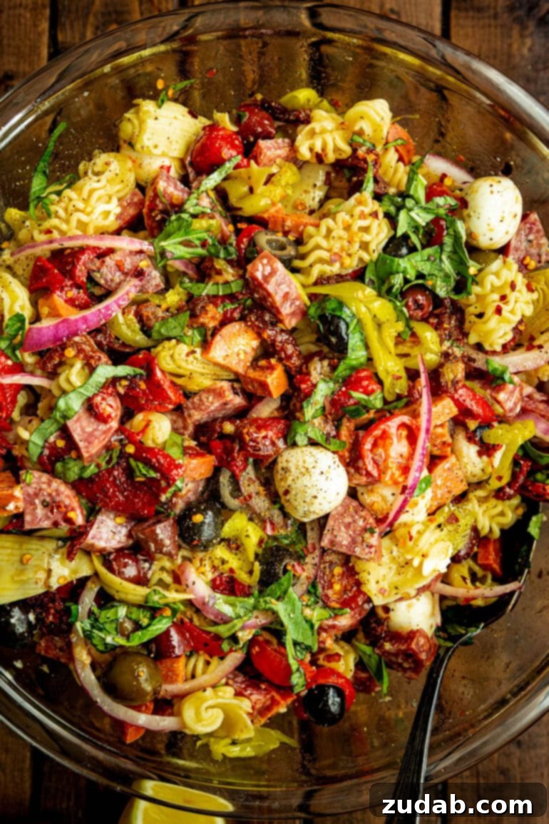 Effortless Antipasto Pasta Salad Recipe 7 A top-down view of a large glass serving bowl brimming with antipasto pasta salad, capturing the vibrant colors and diverse textures of the pasta, meats, cheeses, and various vegetables, all glistening with dressing.