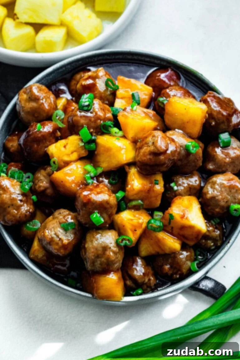 Slow Cooker Island Glazed Meatballs 2 A vibrant plate of saucy Hawaiian meatballs, generously mixed with golden pineapple chunks and fresh green onions, ready to be enjoyed.