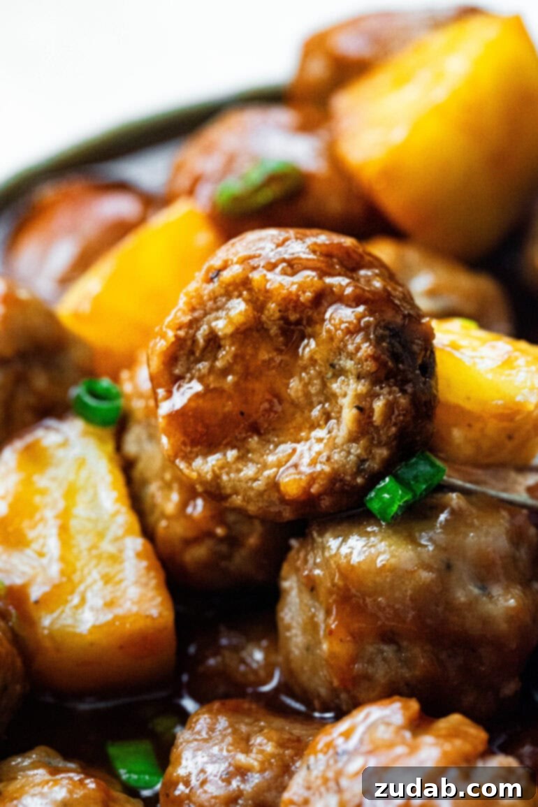 Slow Cooker Island Glazed Meatballs 4 A close-up shot revealing the tender cross-section of a Hawaiian meatball, surrounded by other saucy meatballs and bright pineapple pieces, highlighting its juicy interior.