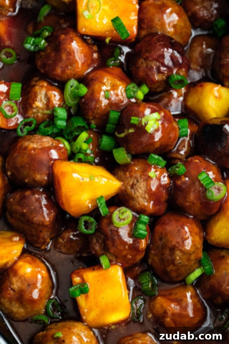 Slow Cooker Island Glazed Meatballs 6 A large, steaming pot of saucy Hawaiian meatballs, brimming with pineapple chunks and garnished with vibrant chopped green onions, ready to be served.