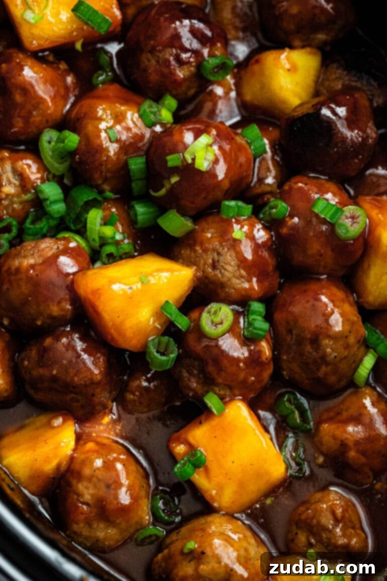 Slow Cooker Island Glazed Meatballs 8 A mouth-watering close-up of juicy, saucy Hawaiian meatballs, beautifully intertwined with sweet pineapple chunks and garnished with a sprinkle of fresh green onions, showcasing their rich texture and vibrant colors.