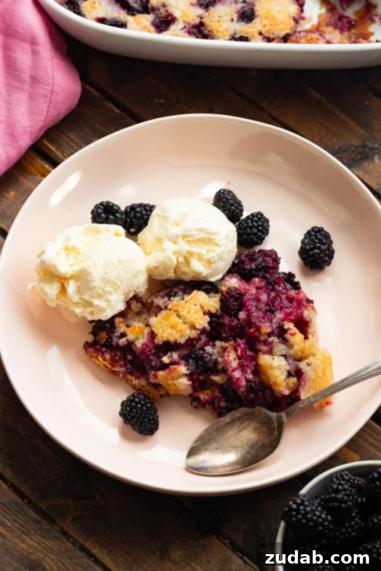 Timeless Blackberry Cobbler Bliss 11 A serving of blackberry cobbler on a small dessert plate, beautifully arranged with fresh blackberries scattered around it and two scoops of vanilla ice cream on the side, highlighting its rustic elegance.