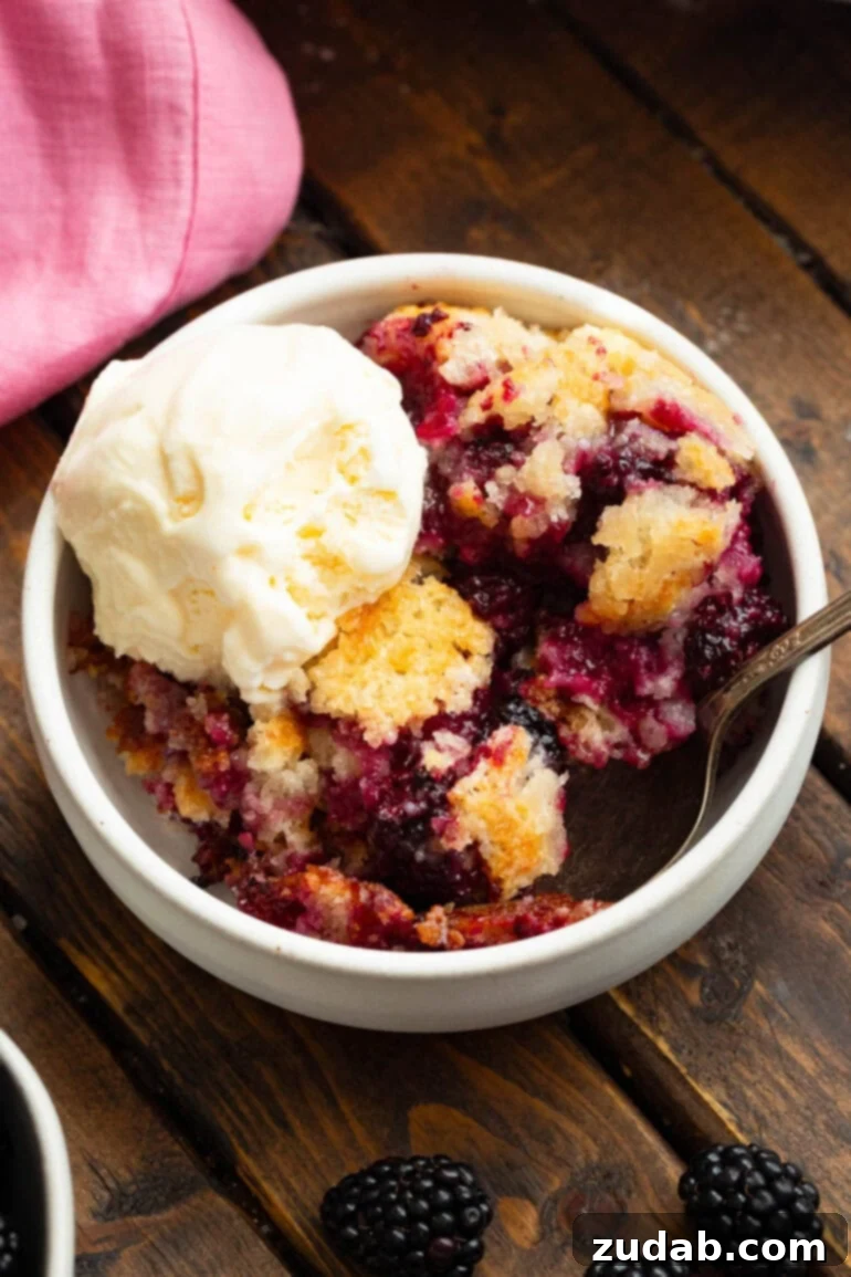 Timeless Blackberry Cobbler Bliss 12 A small bowl filled with a serving of blackberry cobbler, richly topped with a scoop of vanilla ice cream, capturing its irresistible warmth and sweetness.