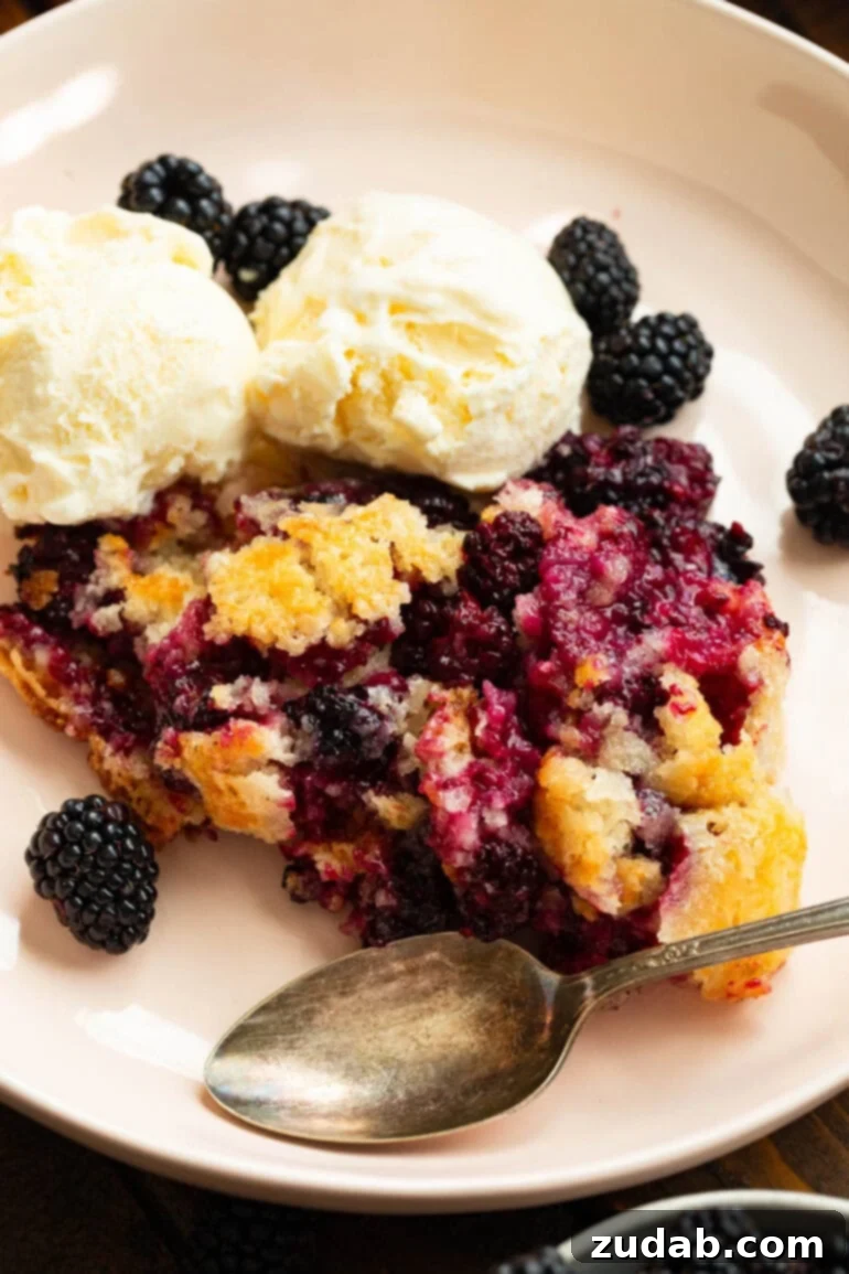 Timeless Blackberry Cobbler Bliss 8 A serving of blackberry cobbler on a small dessert plate, accompanied by fresh blackberries and two scoops of vanilla ice cream on the side, creating an inviting presentation.