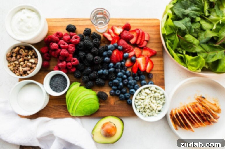 Fresh & Fit Berry Avocado Chicken Salad 4 A flat lay photo of all the wholesome ingredients for Berry Avocado Chicken Salad, including a vibrant array of fresh blueberries, strawberries, blackberries, raspberries, creamy avocado, crumbled blue cheese, and crisp lettuce leaves.