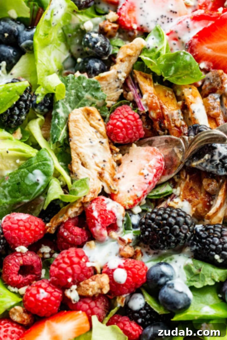 Fresh & Fit Berry Avocado Chicken Salad 6 A close-up view of a perfectly tossed Berry Avocado Chicken Salad, highlighting strips of chicken breast, glistening candied pecans, fresh berries, and a creamy poppyseed dressing.