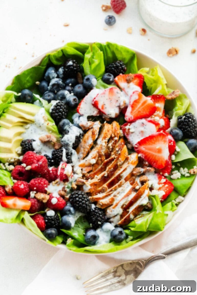 Fresh & Fit Berry Avocado Chicken Salad 9 An inviting overhead shot of a large bowl of Berry Avocado Chicken Salad, complete with sliced grilled chicken, a medley of fresh berries, creamy avocado, and a delicate drizzle of a creamy poppyseed dressing.