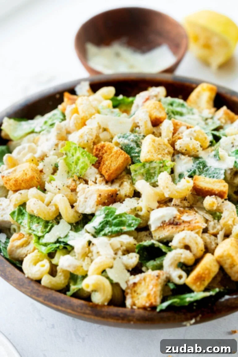Creamy Chicken Caesar Pasta Salad 2 A large wooden serving bowl filled with creamy Chicken Caesar Pasta Salad, garnished with fresh herbs and shaved Parmesan.