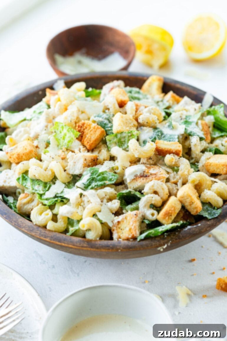 Creamy Chicken Caesar Pasta Salad 6 A large wooden serving bowl filled with a creamy Chicken Caesar Pasta Salad, glistening with homemade dressing and crunchy croutons.