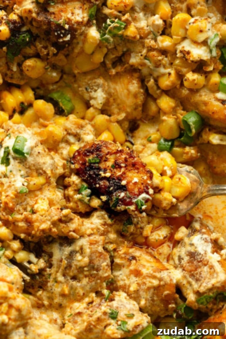 One-Pan Mexican Elote Chicken 11 a photo of a piece of golden brown chicken being scooped up from a dish full of creamy mexican street corn chicken