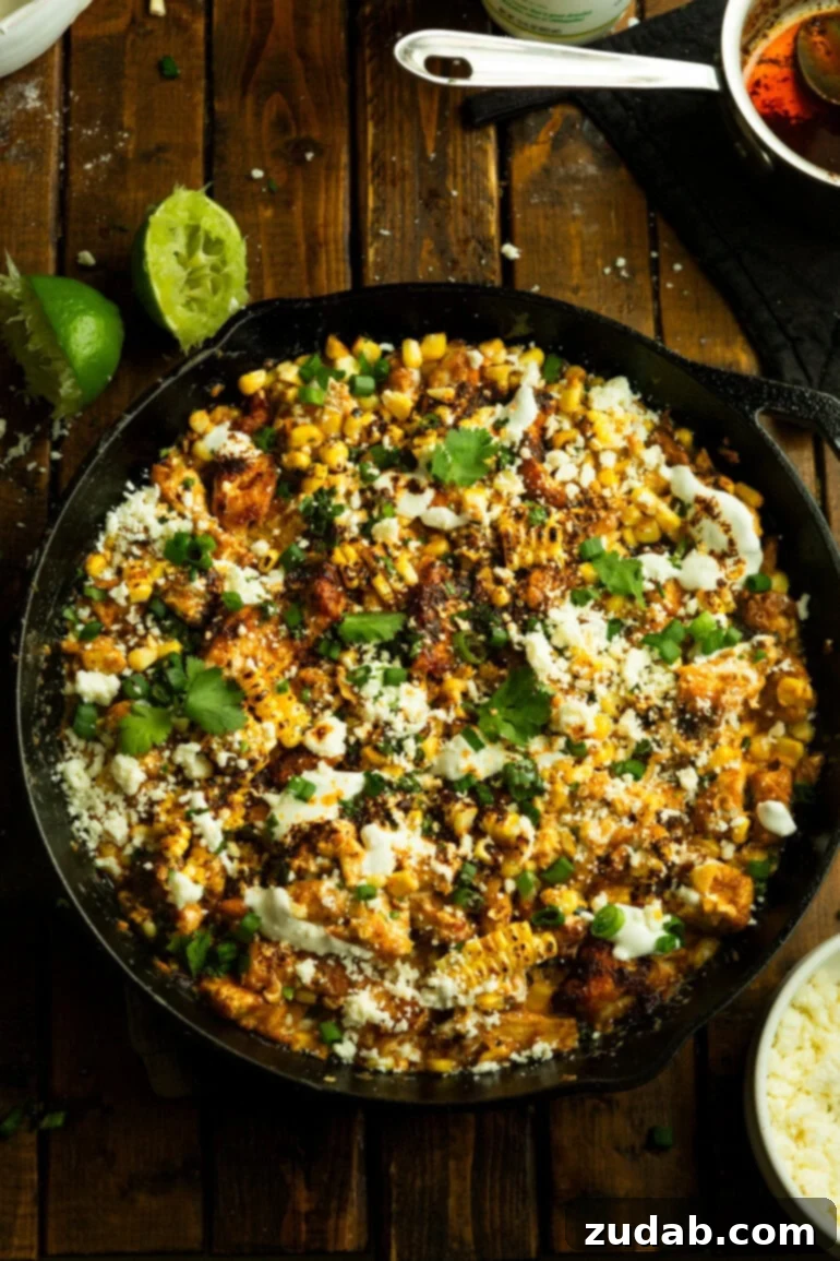 One-Pan Mexican Elote Chicken 12 a photo taken over the top of a cast iron skillet filled with chunks of tender cooked chicken mixed with charred mexican street corn topped with cilantro