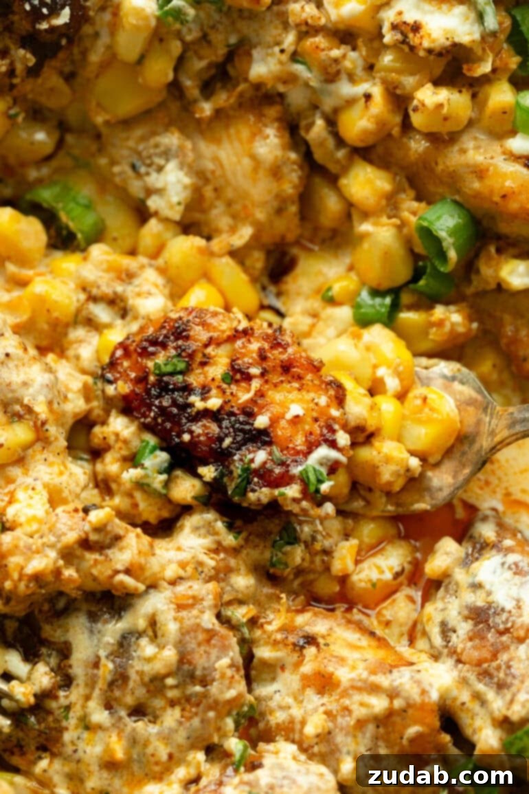 One-Pan Mexican Elote Chicken 8 a photo of a scoop of mexican street corn chicken being lifted from a cast iron skillet full of it