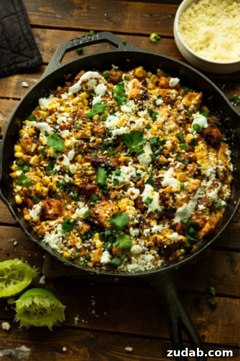 One-Pan Mexican Elote Chicken 9 a photo of a cast iron skillet full of creamy mexican street corn chicken topped with crumbled cotija cheese and chopped cilantro