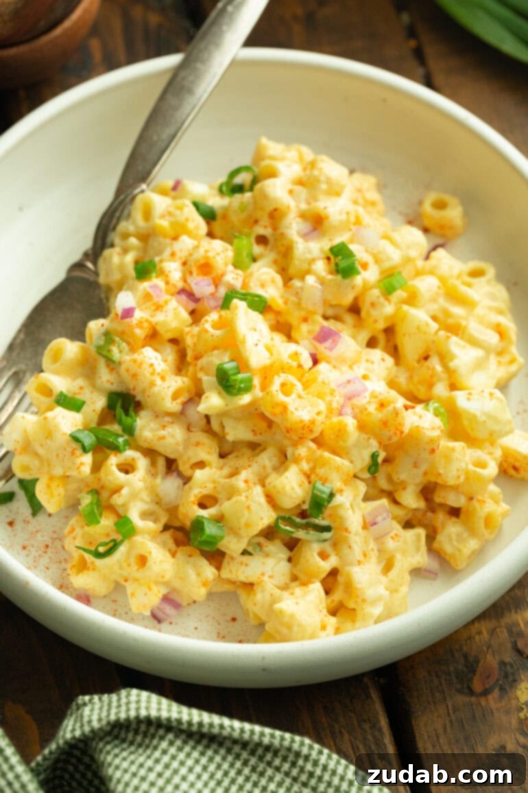 Zesty Deviled Egg Pasta Salad 5 a photo of a serving of deviled egg pasta salad with a fork next to it in a shallow white bowl