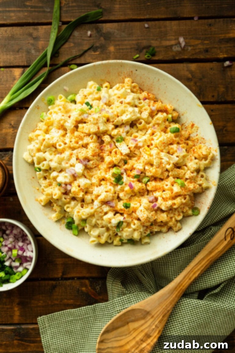 Zesty Deviled Egg Pasta Salad 6 a photo of a large white bowl of creamy deviled egg pasta salad surrounded by a wooden spoon, green onions and the pasta salad garnishes