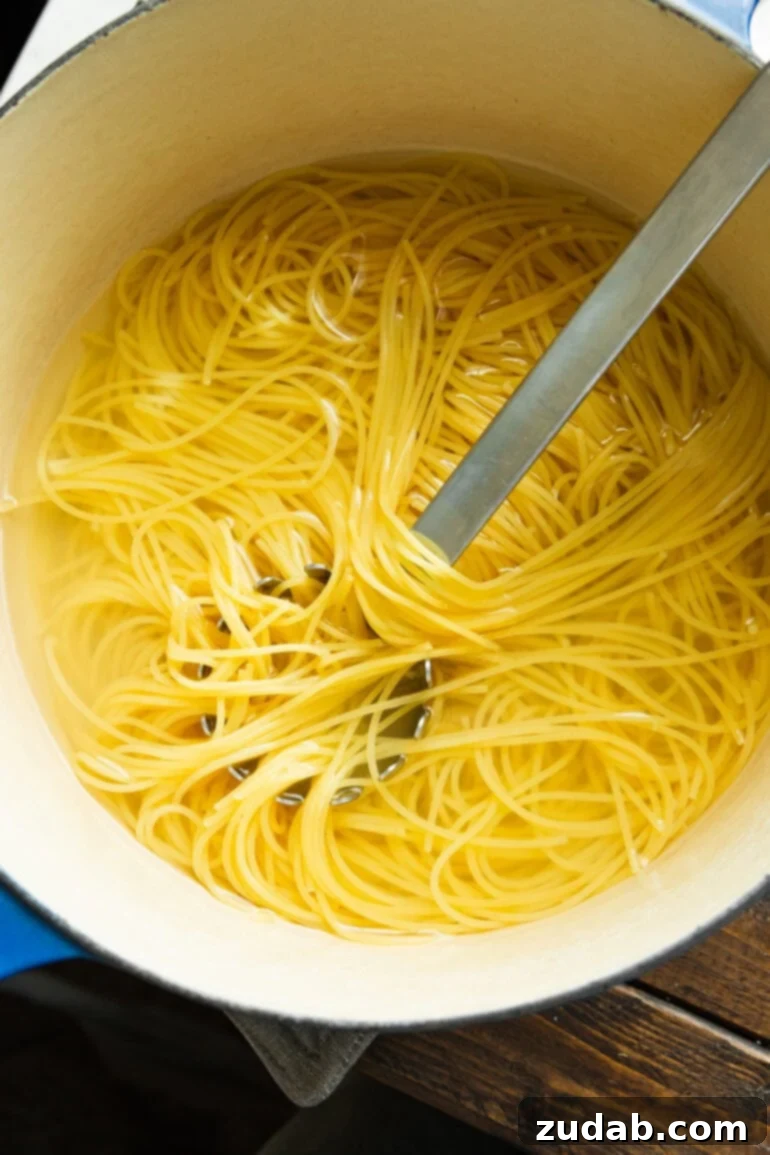 Easy Korean Ground Beef Noodles 6 A large pot of perfectly cooked spaghetti noodles being stirred with a metal spoon, showcasing the ideal al dente texture before mixing with the sauce.