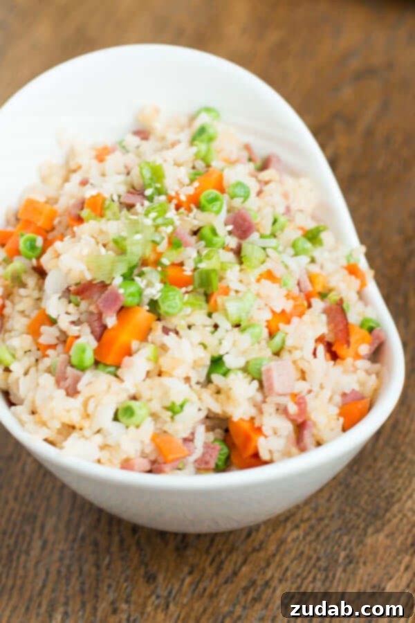 You don't have to even leave your kitchen to have restaurant worthy Chinese food. This is the secret to ham fried rice faux takeout style. A dish of Ham Fried Rice with peas and carrots on a wooden table, ready to be served.