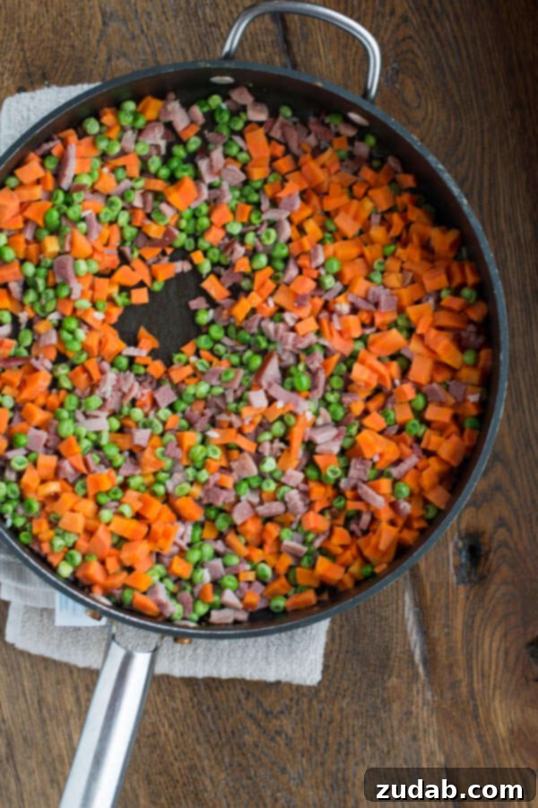 You don't have to even leave your kitchen to have restaurant worthy Chinese food. This is the secret to ham fried rice faux takeout style. Chopped ham, peas, and carrots in a pan, ready to be added to the fried rice.