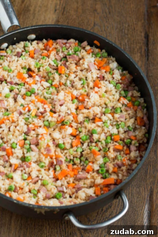 You don't have to even leave your kitchen to have restaurant worthy Chinese food. This is the secret to ham fried rice faux takeout style. Ham Fried Rice cooking in a large pan or wok, showing the mixed ingredients.