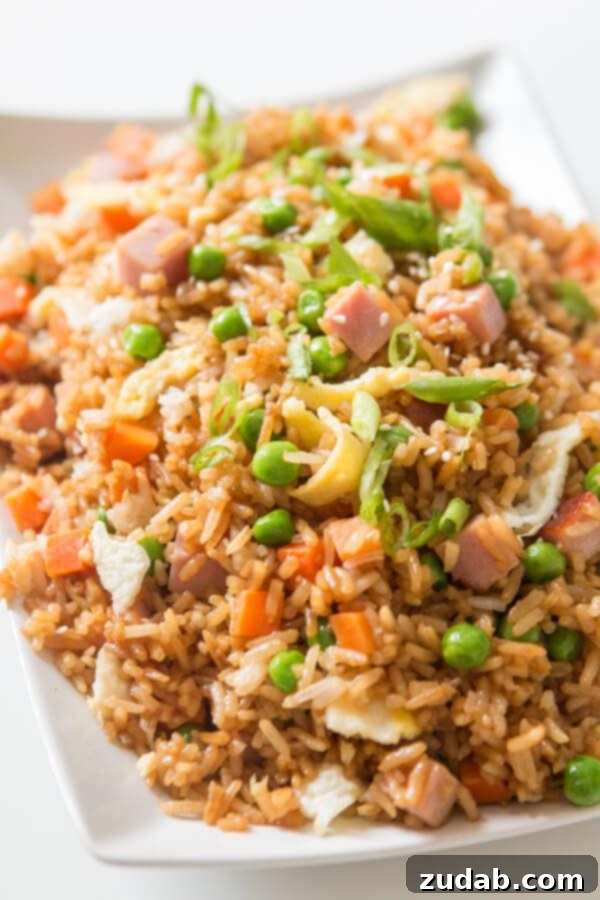 You don't have to even leave your kitchen to have restaurant worthy Chinese food. This is the secret to ham fried rice faux takeout style. A large serving of Ham Fried Rice on a white platter, beautifully garnished and ready to eat.