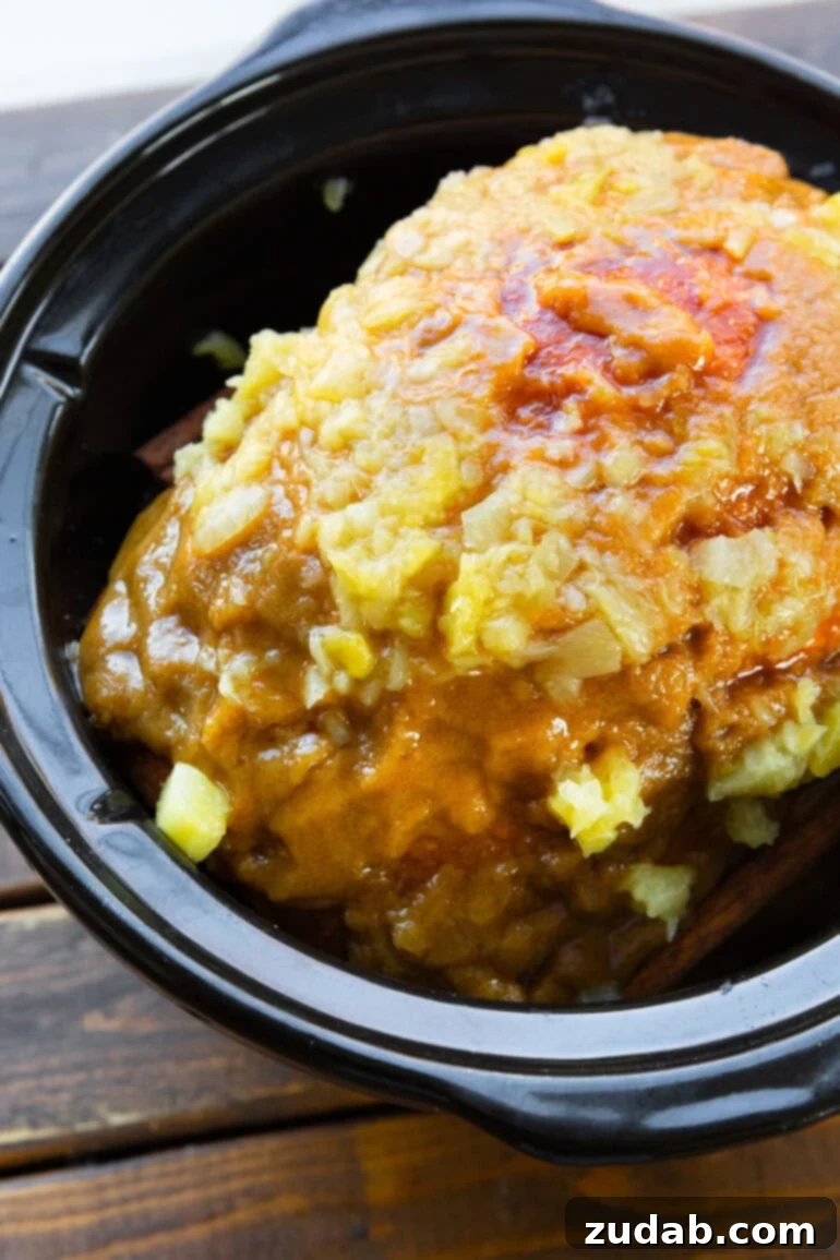 Your New Favorite Slow Cooker Ham 5 a photo of a whole ham sitting in a slow cooker topped with a pineapple glaze