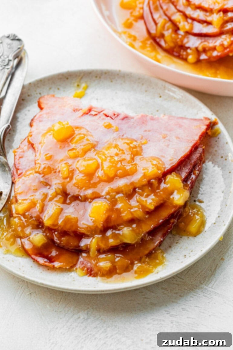 Your New Favorite Slow Cooker Ham 8 a photo of several slices of ham stacked on a white plate topped with a pineapple brown sugar glaze
