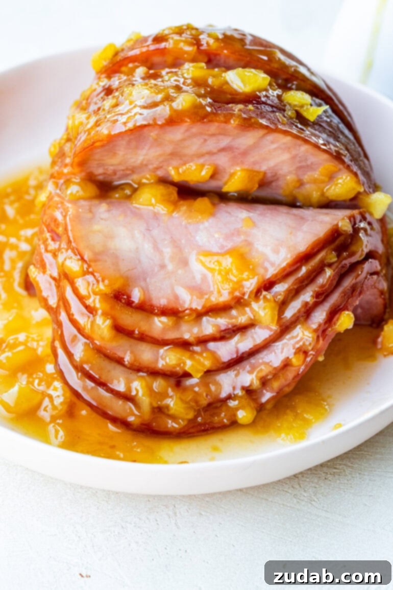 Your New Favorite Slow Cooker Ham 9 a photo of a whole spiral ham sitting on a serving plate topped with a pineapple glaze with several slices fanned down